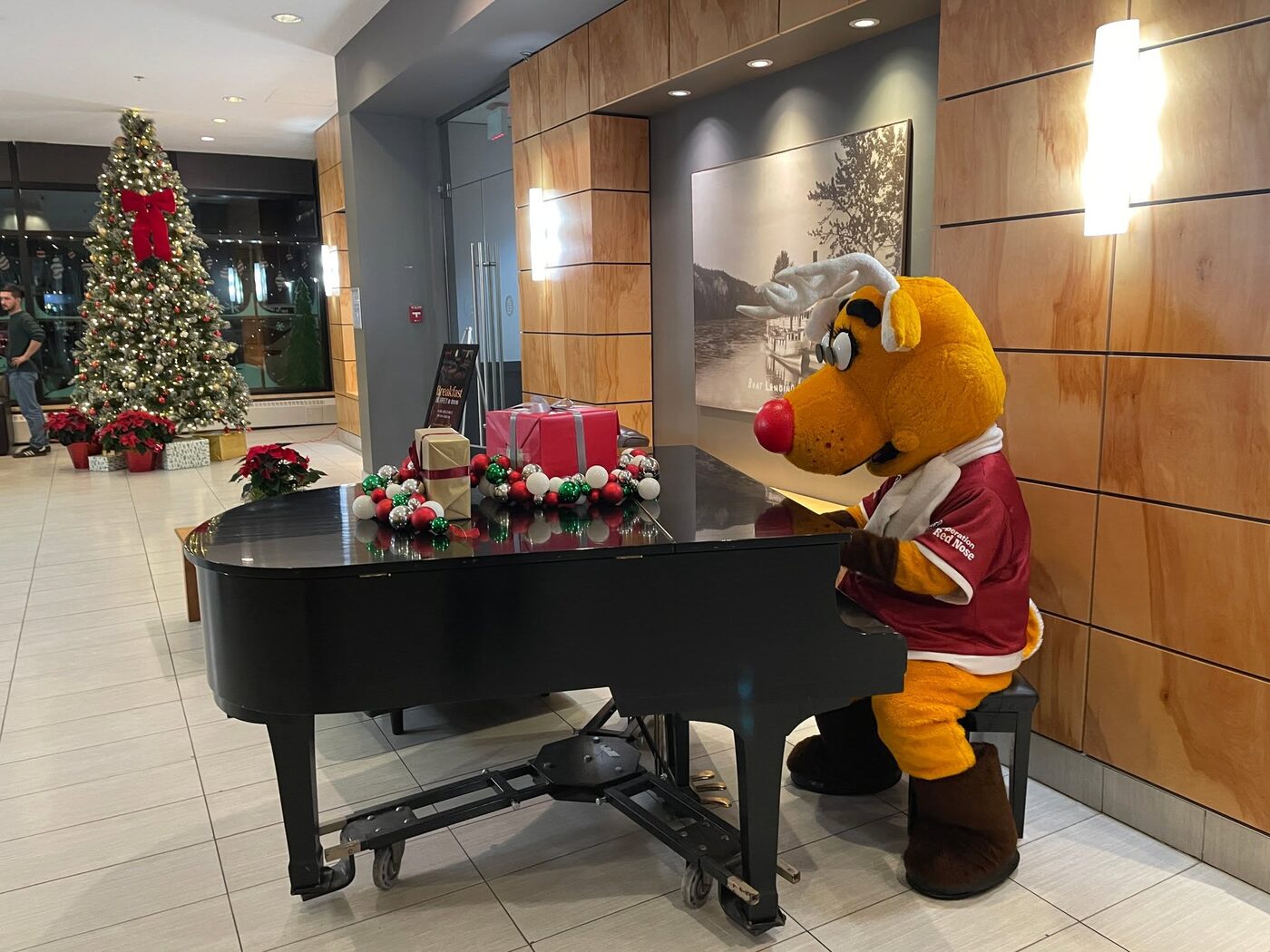 Rudy leaning on a grand piano in a hotel lobby decorated for Christmas.